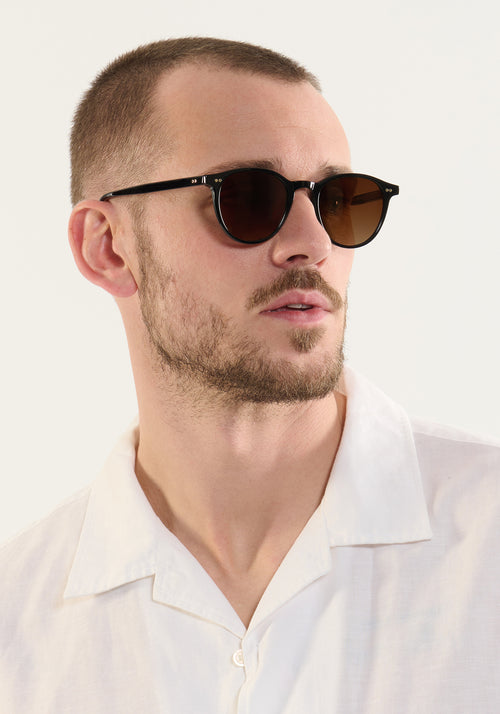 LANDRY | Black + Black Tea Handcrafted, luxury black acetate round KREWE sunglasses mens model | Model: Connor