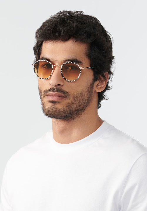 KREWE SUNGLASSES - PORTER | 24K Titanium + Matte Domino + Custom Vanity Tint handcrafted, luxury round black and white spotted sunglasses with orange tinted lenses womens model | Model: Mo