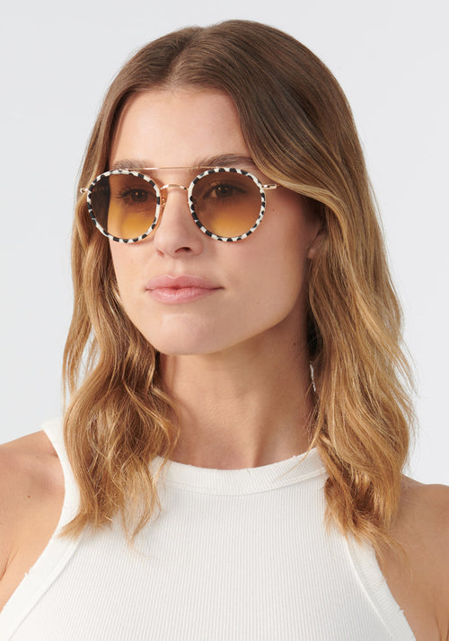 KREWE SUNGLASSES - PORTER | 24K Titanium + Matte Domino + Custom Vanity Tint handcrafted, luxury round black and white spotted sunglasses with orange tinted lenses womens model | Model: Keke